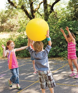 One boy and two girls playing with a big yellow ball.