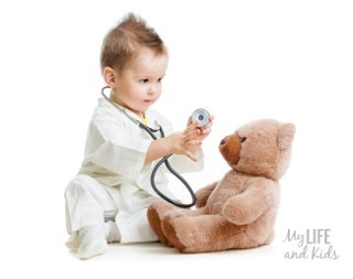 Toddler holding a stethoscope playing doctor with his brown stuffed teddy bear