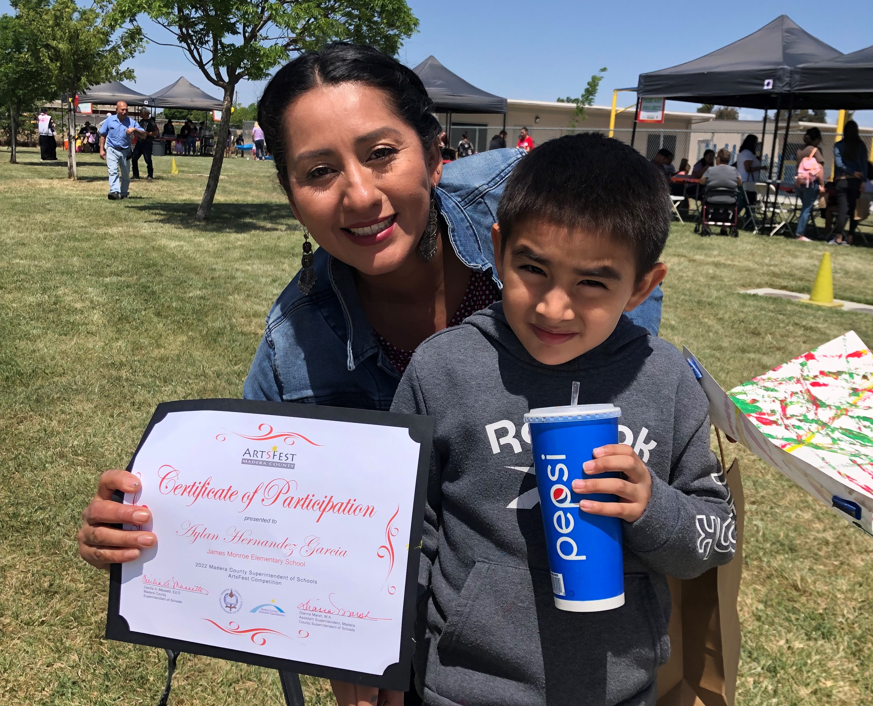 Woman holding a certificate smiling with boy holding drink